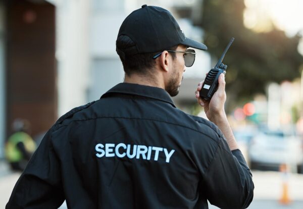 Radio, man and a security guard or safety officer outdoor on a city road for communication. Back of a person with a walkie talkie on urban street to report crime for investigation and surveillance.